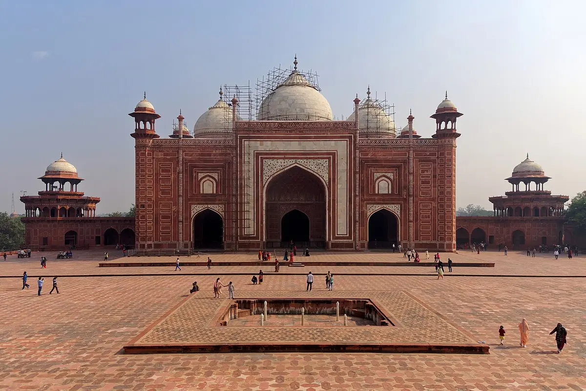 The red sandstone jawab building with white marble domes and a wide courtyard in front, with scaffolding on its domes